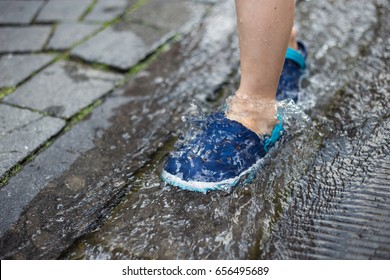 Child in blue rubber shoes walking in the water on warm summer day. Feet in the water.