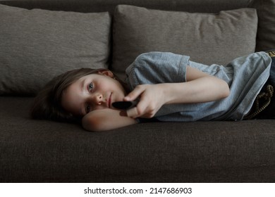 The Child Is Bored At Home Lying On The Couch And Watching TV All Day