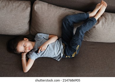 The Child Is Bored At Home Lying On The Couch And Watching TV All Day