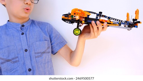 child, boy of 10 years old plays with orange airplane from lego parts, constructor in children's hands close-up, educational toy, concept development fine motor skills, children's entertainment - Powered by Shutterstock