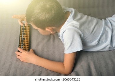 Child Boy 6-7 Years Old Lying On Couch, Counts On Abacus. Mental Arithmetic, Early Child Development