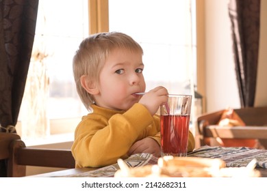 Child Boy With Blonde Hair Baby Drinking Lemonade In Cafe. 3 Years Old Kid Drinks Red Juice From Glasses Through Straws. Boy Toddler In A Restaurant. Closeup Natural Emotion Vintage Portrait.