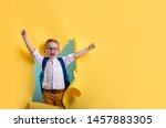 Child boy with book and bag breaking through yellow paper wall. Happy 
smiling kid go back to school, kindergarten. Success, motivation, winner, genius concept. Little kid dreaming to be superhero