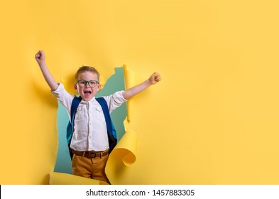 Kinderjunge mit Buch und Tasche, die durch gelbe Papierwand zerbricht. Fröhlich 
lächelndes Kind zurück in die Schule, Kindergarten. Erfolg, Motivation, Sieger, geniales Konzept. Kleines Kind träumt, Superheld zu sein