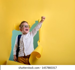 Child boy with book and bag breaking through yellow paper wall. Happy 
smiling kid go back to school, kindergarten. Success, motivation, winner, genius concept. Little kid dreaming to be superhero - Shutterstock ID 1457883317