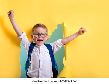 Child boy with book and bag breaking through yellow paper wall. Happy 
smiling kid go back to school, kindergarten.  - Shutterstock ID 1458021764