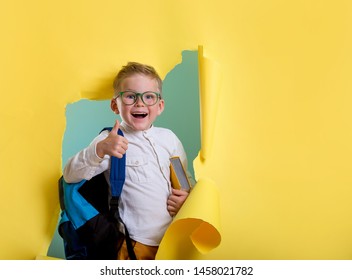 Child Boy With Book And Bag Breaking Through Yellow Paper Wall. Happy 
Smiling Kid Go Back To School