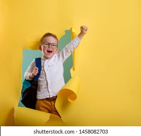Child boy with book and bag breaking through yellow paper wall. Happy 
smiling kid go back to school, kindergarten.  - Shutterstock ID 1458082703