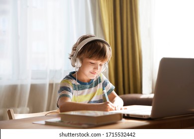 child boy in earphones is using a laptop and study online at home. homeschooling, distant learning