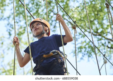 Child Boy Enjoys Climbing In The Ropes Course Adventure. Child Engaged Climbing High Wire Park. Active Brave Little Boy Enjoying Climbing At Treetop Adventure Park