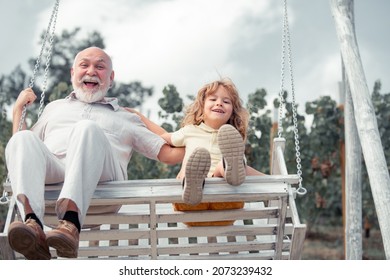 Child Boy And Grandfather Swinging In Summer Garden. Grand Dad And Grandson Sitting On Swing In Park. Generations Ages.