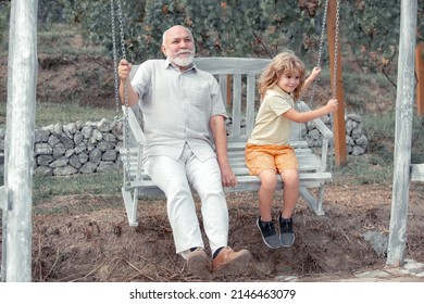 Child boy and grandfather swinging in summer garden. Grand dad and grandson sitting on swing in park. Generations ages.