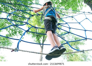 Child boy having summer fun at adventure park on the zip line. Balance beam and rope bridges