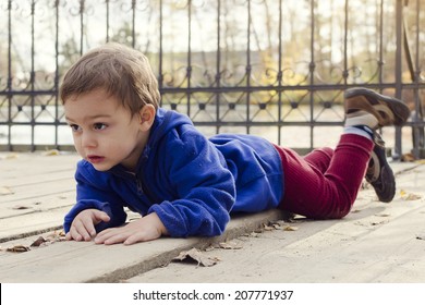 Child Boy Laying On A Wooden Floor Ground On A Bridge Or Landing In Autumn Or Fall Park Outside. 