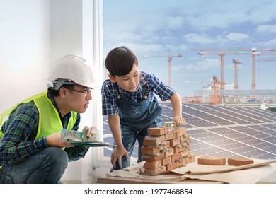 Child boy is learning to install installing brick masonry with an engineer father, Solar panel and crane in the background, Father and son concept
