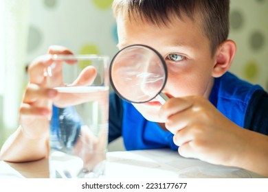 The child boy looking at water in a glass through magnifying glass - Shutterstock ID 2231177677