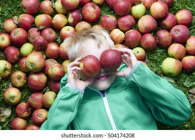 Child boy lying on grass with apples on eyes