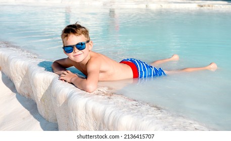 Child Boy In Outdoor Nature Pool In The Background. Happy Boy In Sunglasses Relax In Blue Water. Family Vacation In Luxury Resort. Kids In The White Mountains. Children Swim In Hot Spring