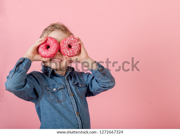 ピンクの背景に子どもの少年とピンクのドーナツ ドーナツを持つ子供 食べ物を食べて楽しい時間を過ごす 幸せな子どもたちは 肥満で食べる おしゃれな子ども の写真素材 今すぐ編集