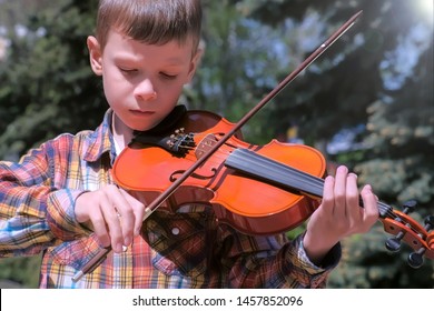 Child Boy Is Playing The Violin Standing In Park In The City. Portrait Of Little Musician. Education Learn Play Violin Boy Teen Violinist Instrumentalist Performance Melody.