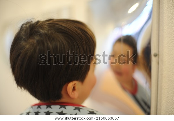 A child boy reflected in diverging mirror,\
spherical mirror creating optical illusion of distorted face and\
shape on the surface of glass