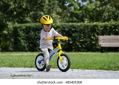 Child Boy Riding On His First Bike With A Helmet. Bike Without Pedals. Child Learning To Ride And Balance On His Two Wheeler Bike With No Pedals.