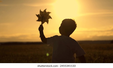 Child boy runs with toy wind pinwheel in his hand on summer field, sun day. Happy child playing with toy pinwheel outdoors in summer in park against sky. Childhood children. Family holiday, nature - Powered by Shutterstock