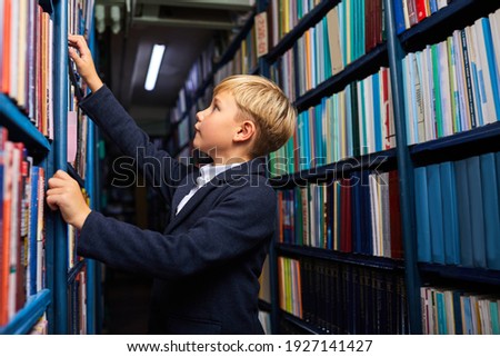 child boy is searching and choosing book in bookshop, stand near shelves, going to learn and study. side view