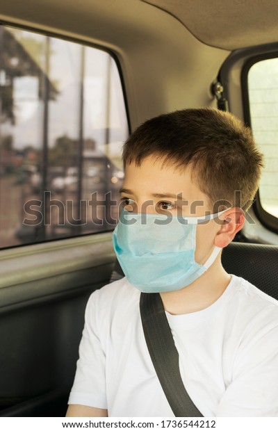 child boy sitting in a car \
in a medical mask on his face as a measure of protection against\
viruses.