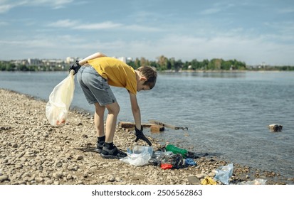 A child boy volunteer in gloves tidying up rubbish plastic garbage from the riverbank. Children take care of nature. - Powered by Shutterstock