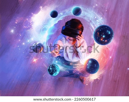 Child boy wearing virtual reality headset and looking at digital space system with planets or Universes. Space exploration with augmented reality glasses. He sits on floor. View above