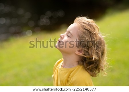 Child breathing fresh air. Child faith, praise and happiness and freedom. Kid resting in summer park. Kid put face to the sun, closed her eyes and feeds energy of nature, dreams.
