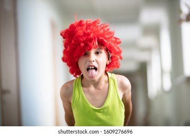 A Child In A Bright Wig. Funny Boy With Red Artificial Hair. Bad Man Shows Tongue.