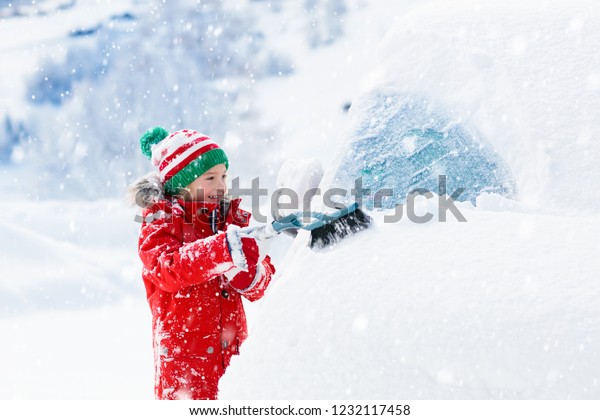 Child brushing snow off car after storm. Kid with
winter brush and scraper clearing family car after overnight snow
blizzard. Family Christmas vacation in the mountains. Kids
shoveling snow.