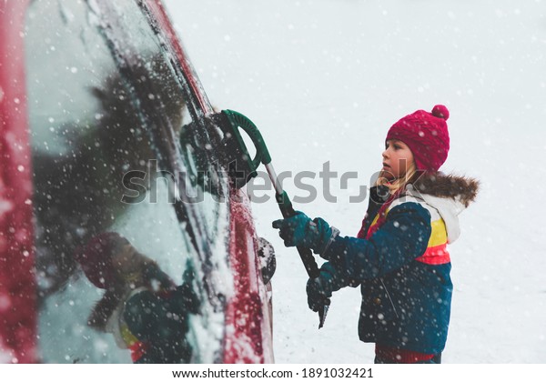 Child brushing snow off car. Kid with winter\
brush and scraper clearing family\
car.