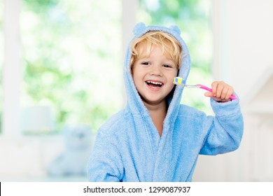 Child Brushing Teeth. Kids Tooth Brush And Paste. Little Baby In Blue Bath Robe Or Towel Brushing His Teeth In White Bathroom With Window On Sunny Morning. Dental Hygiene And Heath For Children.