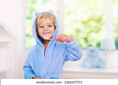 Child Brushing Teeth. Kids Tooth Brush And Paste. Little Baby Boy In Blue Bath Robe Or Towel Brushing His Teeth In White Bathroom With Window On Sunny Morning. Dental Hygiene And Heath For Children.