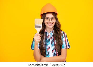 Child Builder In Helmet. Teenage Girl Painter With Painting Brush Tool Or Paint Roller. Child On Repairing Work Isolated On Yellow Background. Kids Renovation Concept.