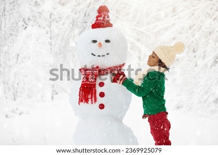 Child building snowman. Kids build snow man. Boy playing outdoors on snowy winter day. Outdoor family fun on Christmas vacation. Children play in beautiful sunny park.