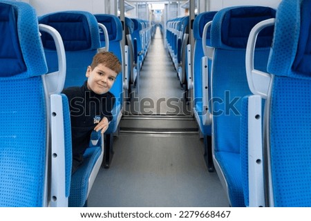 Child in cabin of a passenger train. Empty blue seats inside train cabin, corridor view. Modern european economy class fast train interior. 