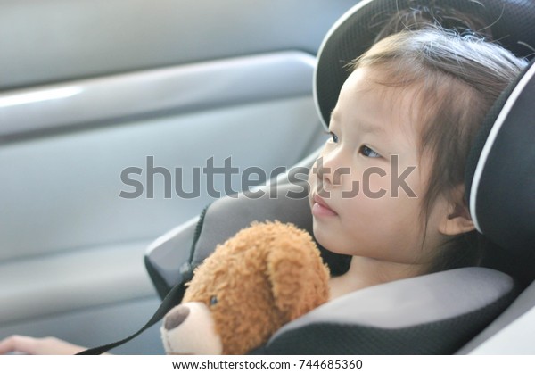 Child in the car seat with\
her bear