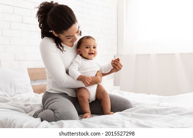 Child Care. African American Mommy Cuddling Her Lovely Infant Baby Son Sitting In Bed Indoors. Mother's Leisure And Lifestyle. Happy Woman Enjoying Motherhood Playing And Bonding With Toddler Boy