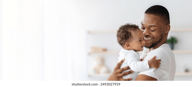 Child Care. Portrait Of Happy African American Father With Infant Baby In Arms Standing Near Window At Home, Young Black Dad Spending Time With Adorable Toddler Child, Panorama With Copy Space - Powered by Shutterstock