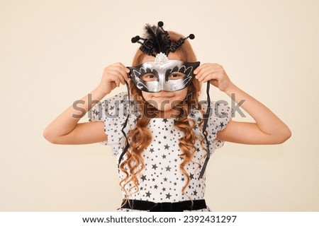Child in a carnival masquerade mask.  Festival, carnival, masquerade, party.  A little cute girl makes faces in a mask.  Black and silver mask