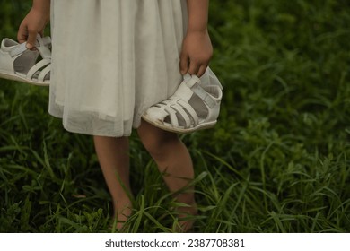 Child carries sandals, the tender grasp suggesting a reluctance to end playtime. Echoes a call to cherish and prolong the fleeting moments of childhood. - Shutterstock ID 2387708381