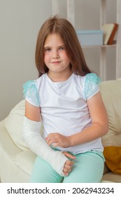 Child With A Cast On A Broken Wrist Or Arm Smiling And Having Fun On A Couch. Positive Attitude, Recovery And Kid Concept.