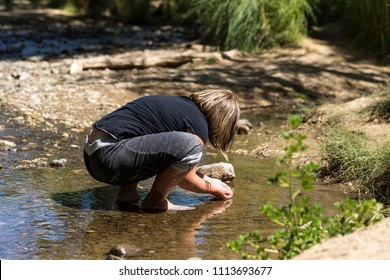 Child Catching Tadpoles In A Rock Bottomed Creek