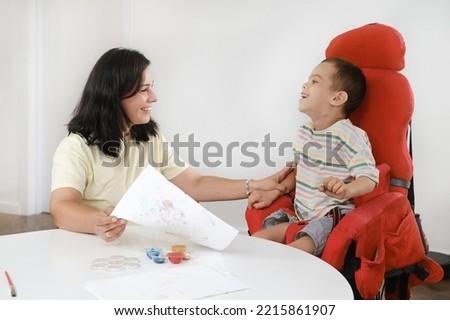 Child with cerebral palsy painting with fingers and hands boy that has health problems developing fine motor skills Education for children with mental, physical disorders, sensory art therapy