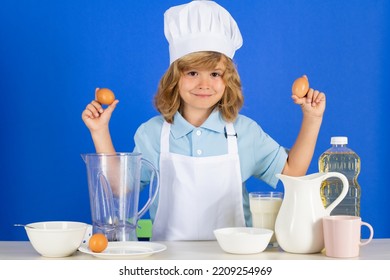 Child Chef Cook Hold Eggs Prepares Food In Isolated Blue Studio Background. Kids Cooking. Teen Boy With Apron And Chef Hat Preparing A Healthy Vegetables Meal In The Kitchen.