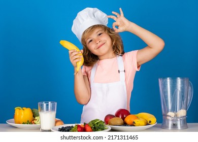 Child Chef Cook Prepares Food Hold Banana In Isolated Blue Studio Background. Kids Cooking. Teen Boy With Apron And Chef Hat Preparing A Healthy Vegetables Meal In The Kitchen.